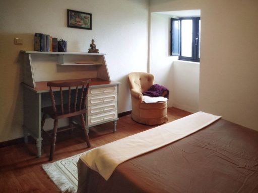 Habitación sencilla con escritorio, silla y un sillón cerca de la ventana.