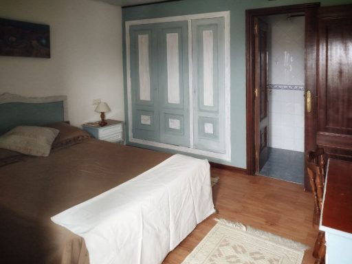 Habitación con cama, mesita de noche y puerta hacia un baño. Decoración en tonos suaves.