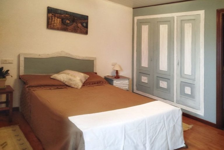 Dormitorio con cama matrimonial, muebles claros y armario de puertas blancas y azules.