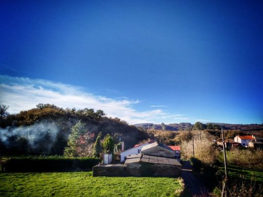 Paisaje rural con una casa, montañas y cielo despejado. Humo saliendo de una chimenea.