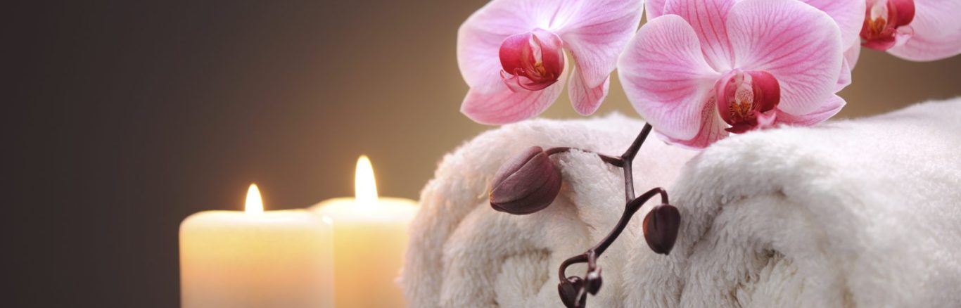 Ramo de orquídeas rosas junto a velas encendidas y una toalla blanca.