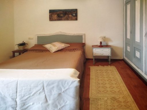 Habitación con cama beige, mesita de noche y armario azul claro. Suelo de madera.